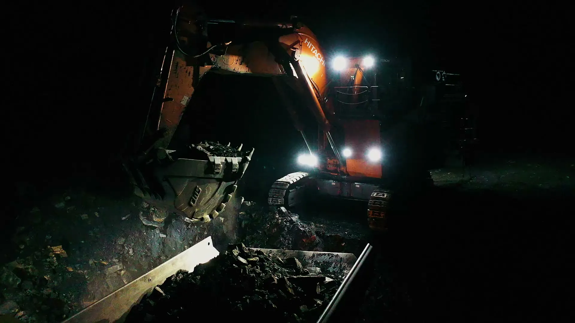 EX2000 excavator dumping a bucket under work lights at night