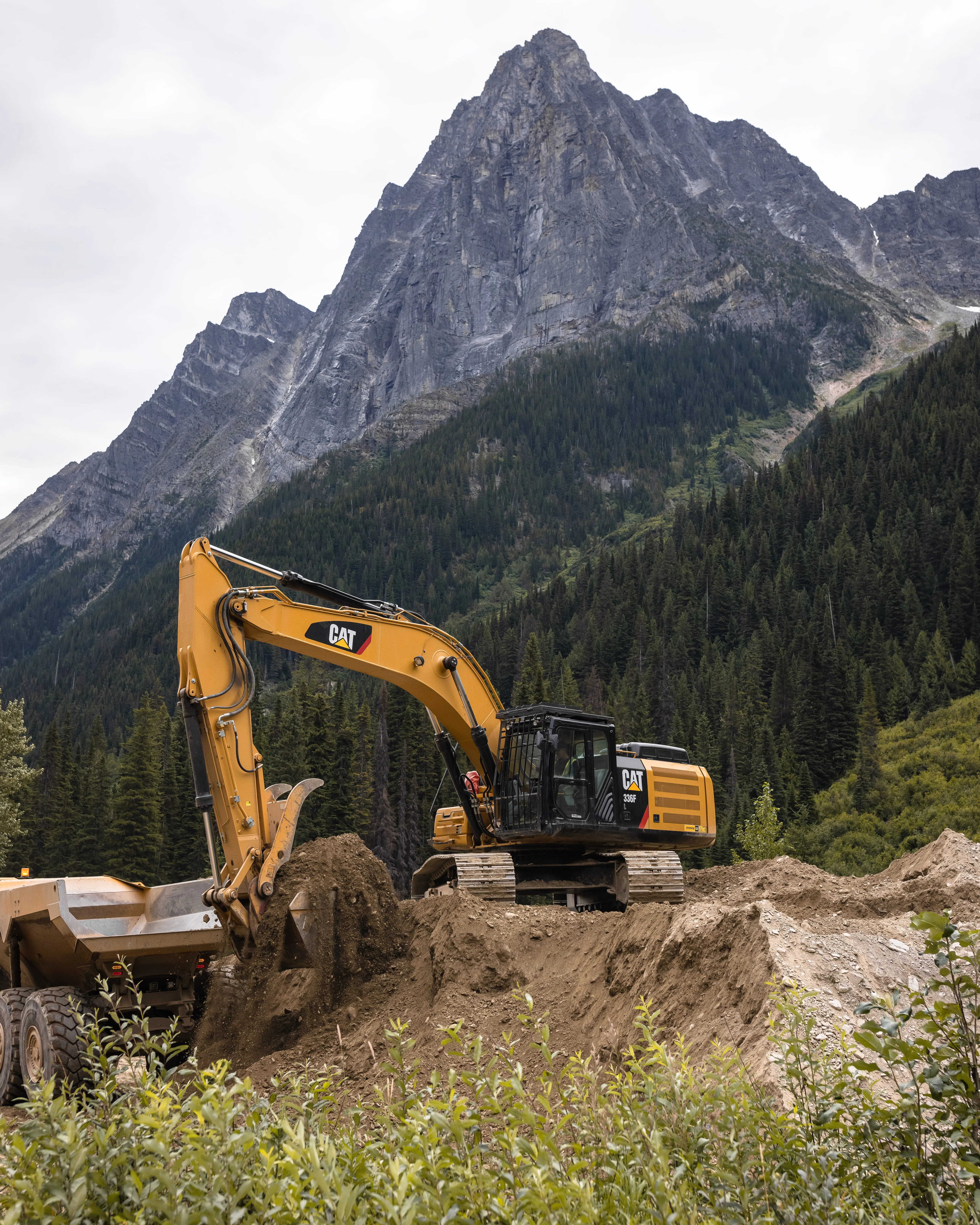 Excavator shaping an avalanche berm beneath a mountain peak