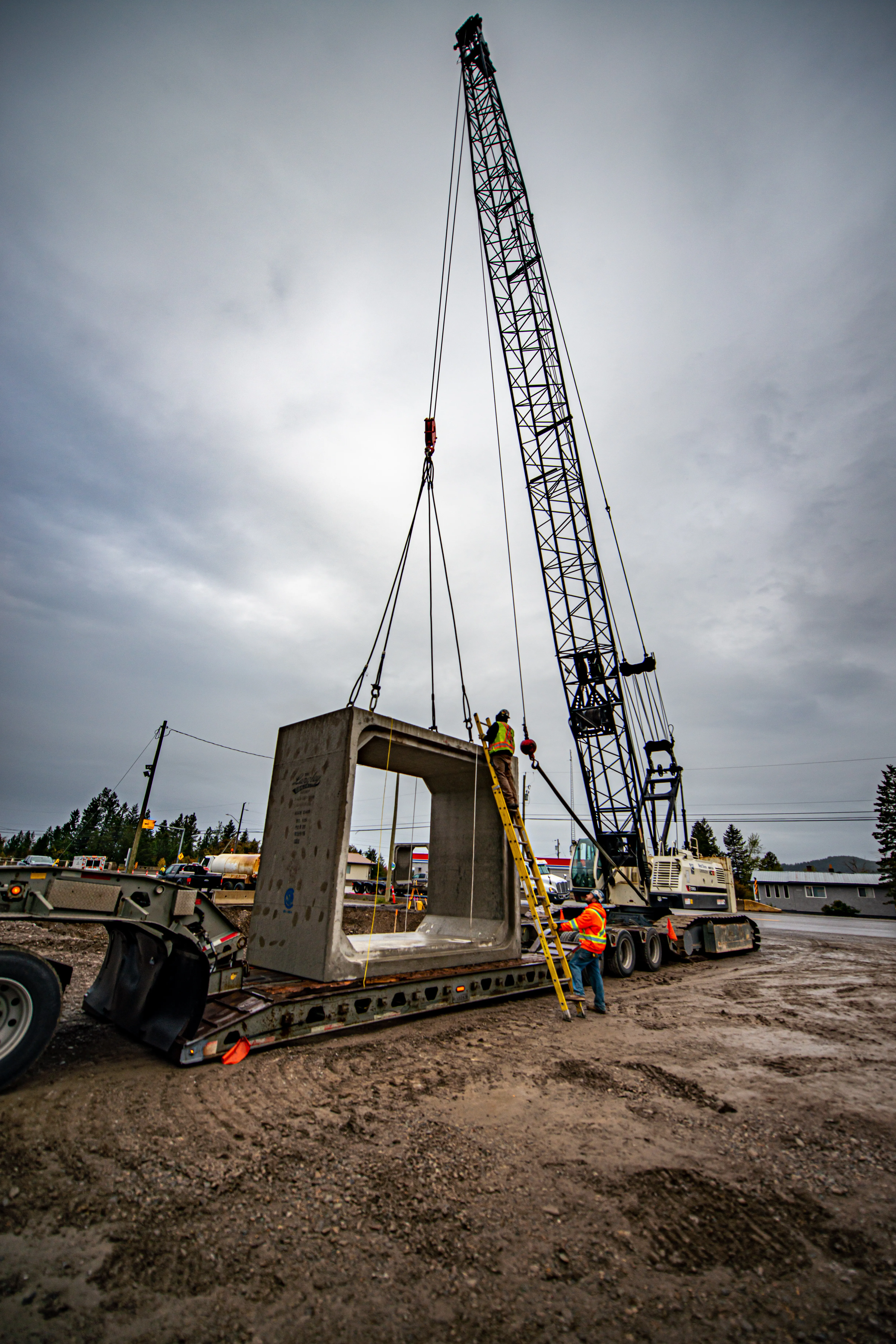 Crane rigging a precast box culvert while a worker connects the lift from a ladder