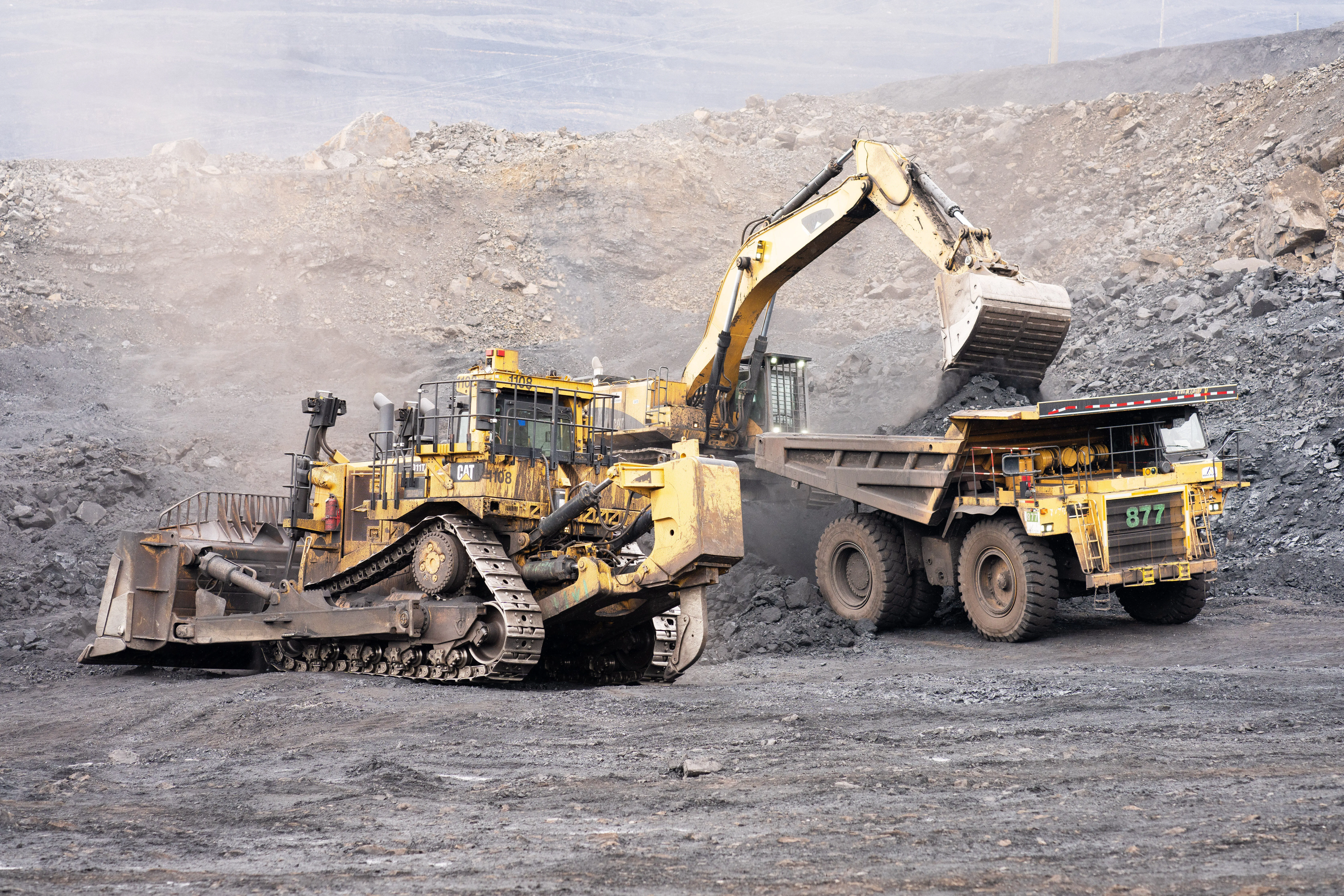 Excavator loading a haul truck with mountain peaks behind