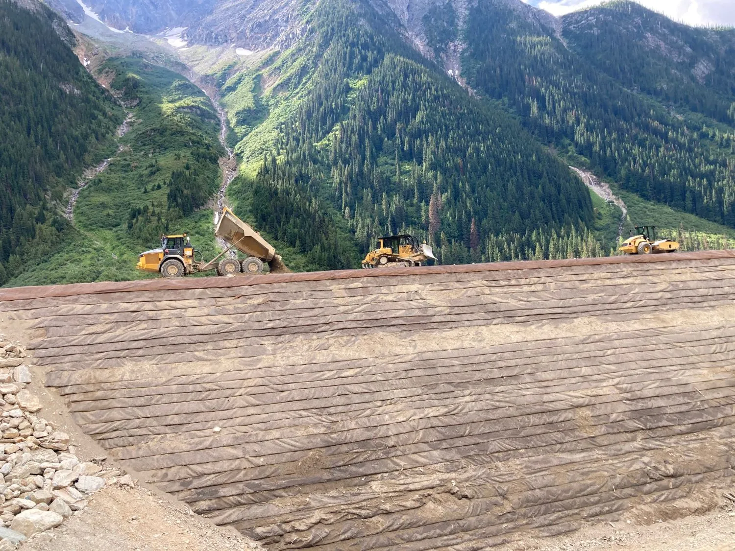 Haul truck, dozer, and packer working the crest of the reinforced avalanche berm below the slide path