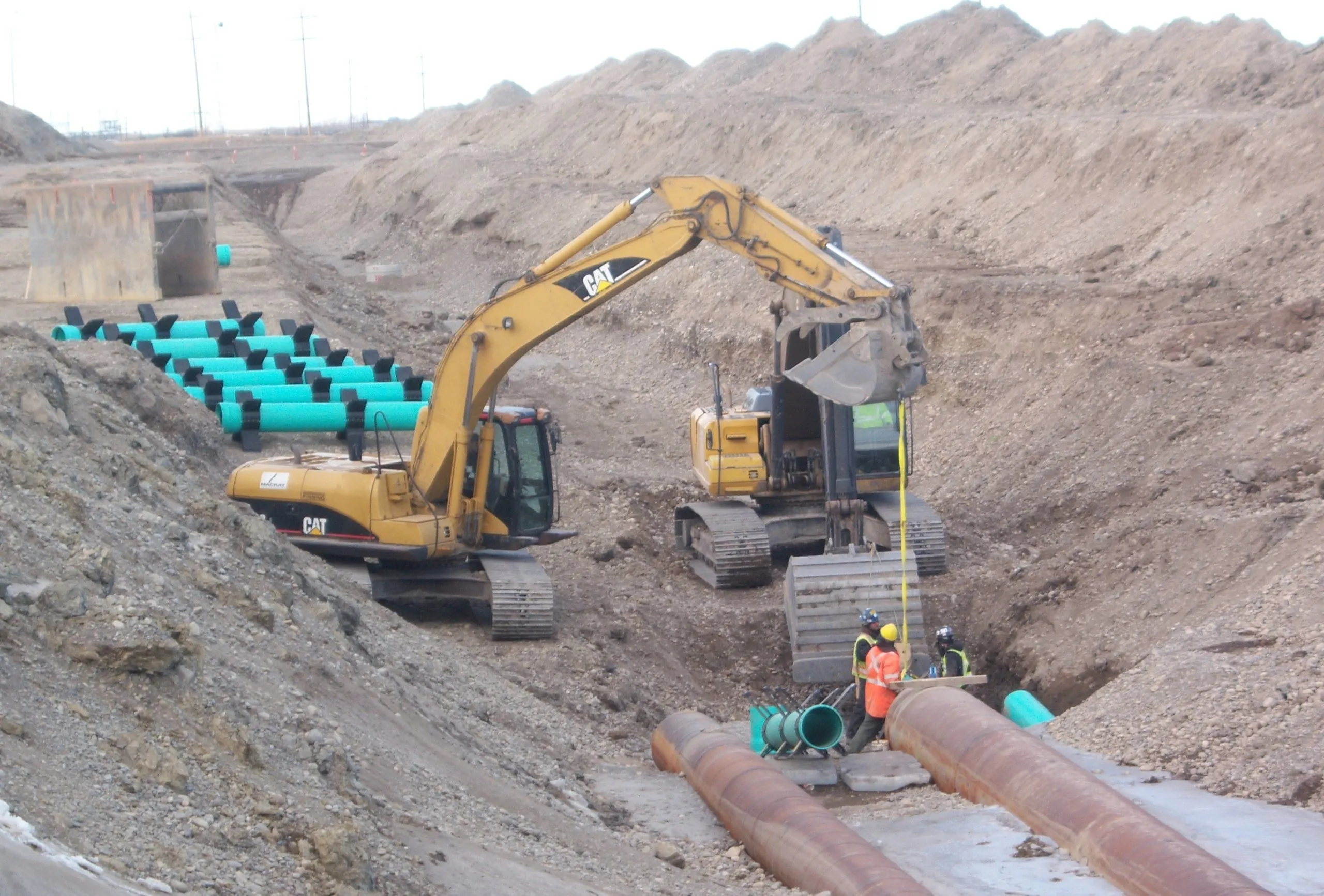 Excavator placing large-diameter watermain pipe in a deep trench