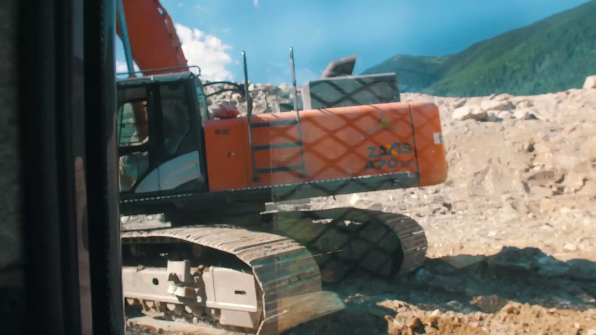 Excavator working a rocky bench, seen through the cab glass