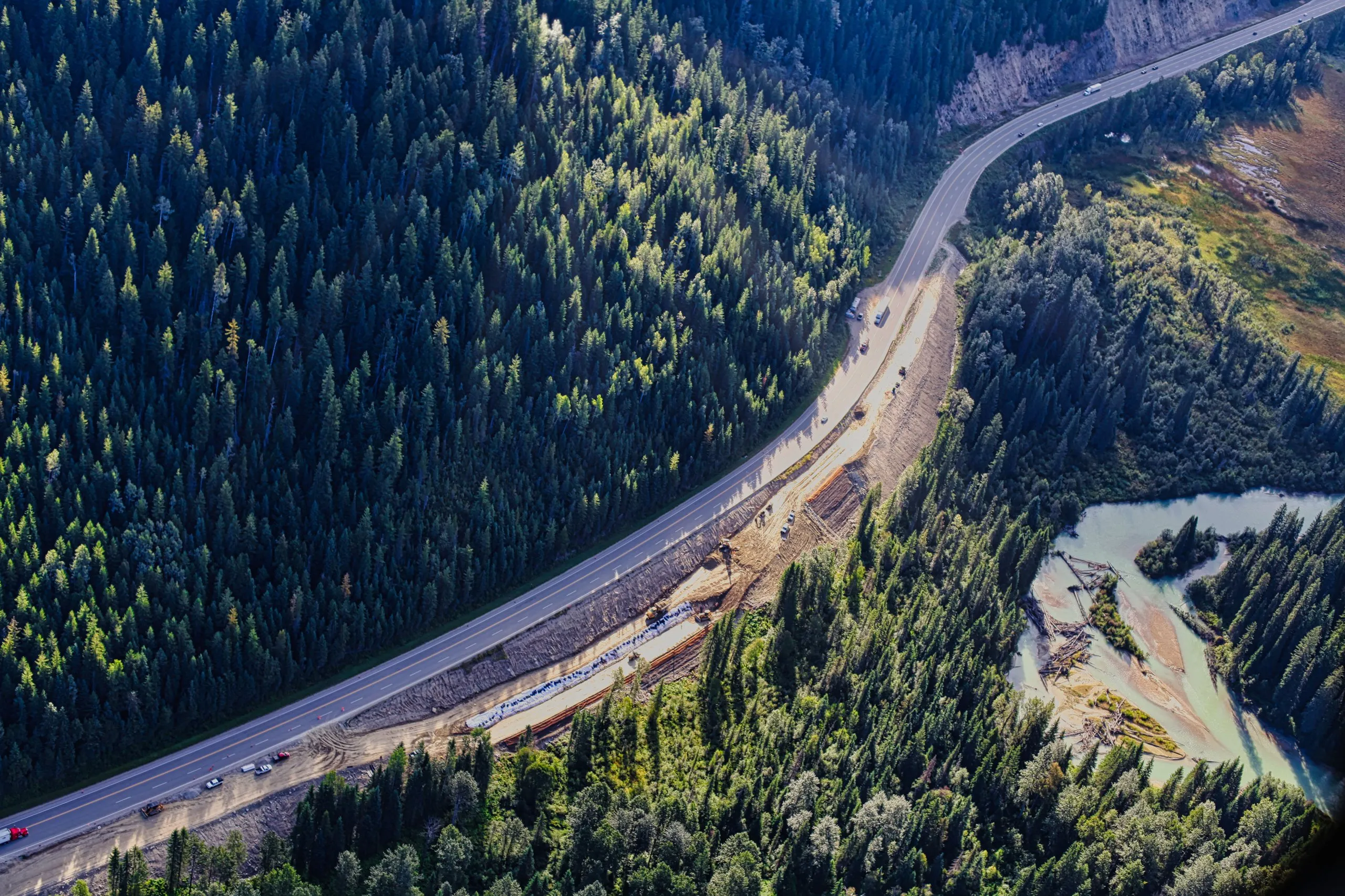 Aerial view of a highway corridor winding through forest beside the river